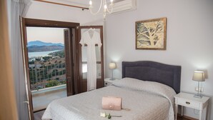 A bedroom with a large bed, a nightstand with a lamp, a view of the outdoors, and a painting on the wall. - Villa Imperia 3 bedroom luxury villa - 200m from the beach (Elounda)