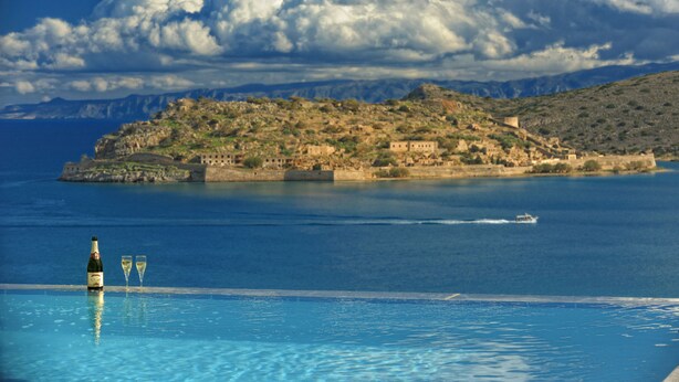 A pool with a bottle and glasses, a boat on the water, and a distant island with buildings. - Villa Imperia 3 bedroom luxury villa - 200m from the beach (Elounda)