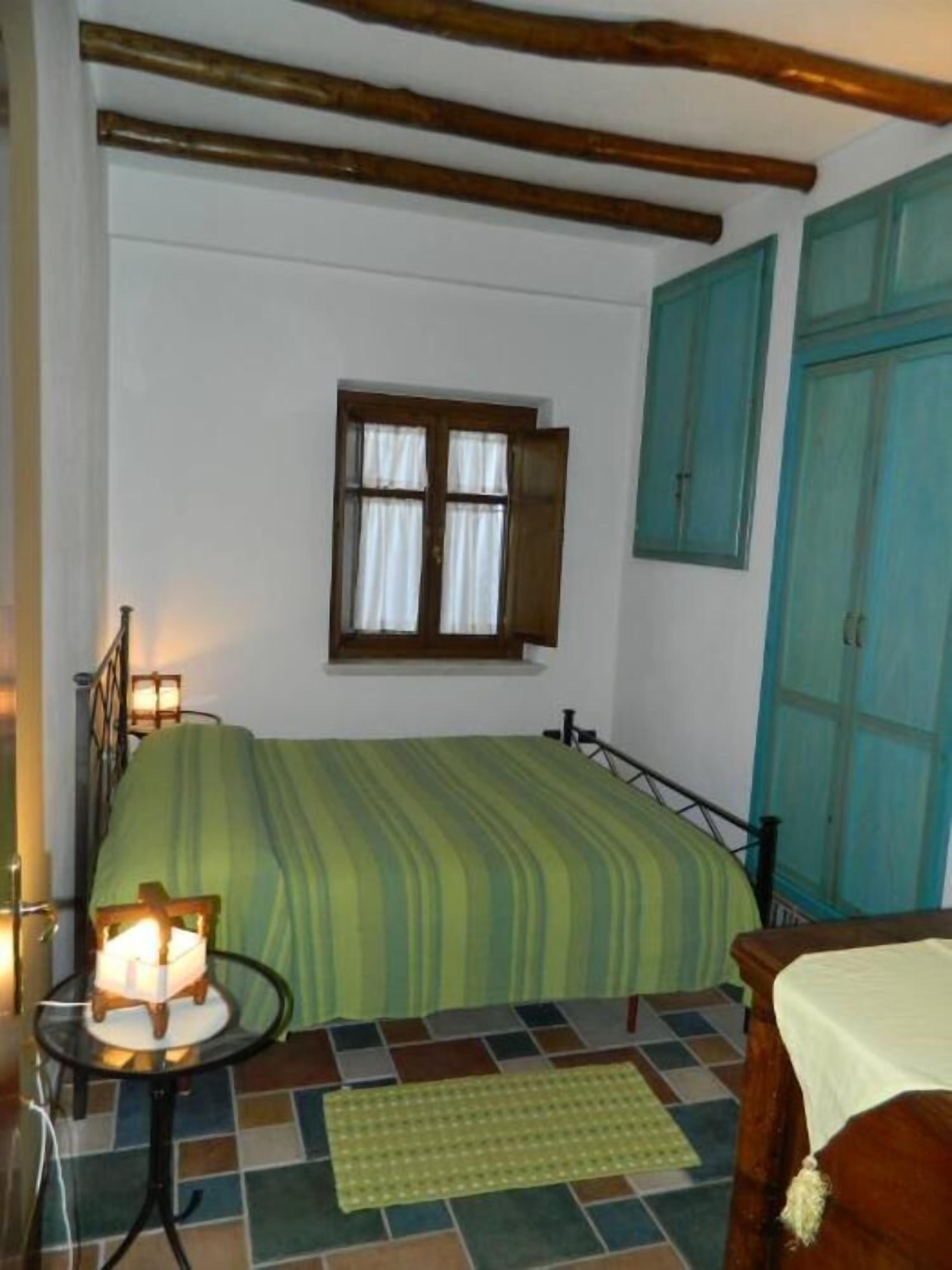 Una stanza con un letto, una finestra, una coperta a righe verdi, un tappeto verde, una testiera in legno e un armadio verde acqua.