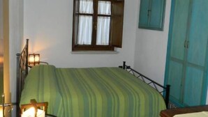 A room with a bed, a window, a green-striped bedspread, a green rug, a wooden headboard, and a teal-colored wardrobe. - HOUSE WITH VERANDA AT A FEW STEPS FROM THE SEA (Santa Maria Navarrese)