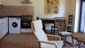 A compact kitchen with a washing machine, oven, and a dining area with chairs and a table.