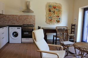 Cozinha compacta com máquina de lavar, forno e área de refeições com cadeiras e mesa.