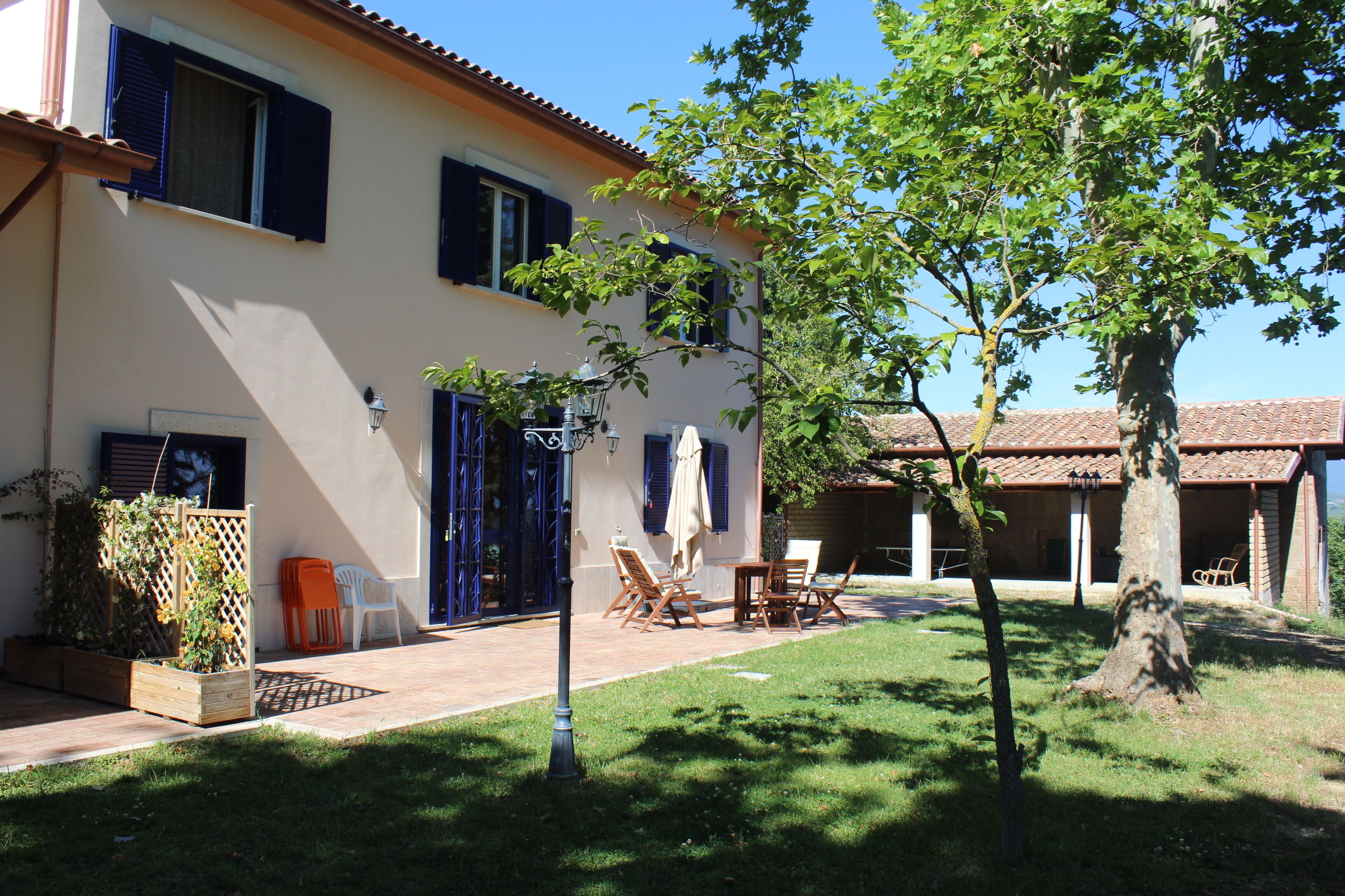 Ein zweistöckiges Haus mit Terrasse, Gartenmöbeln und einem Baum.