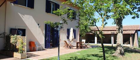 Ein zweistöckiges Haus mit Terrasse, Gartenmöbeln und einem Baum.