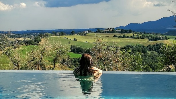 A person sitting in a pool with a view of a green landscape and mountains.