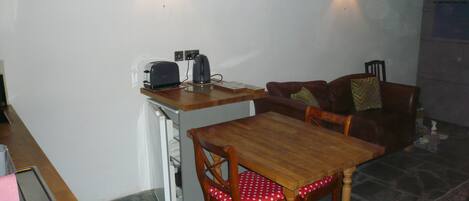 Een knus woongedeelte met een eettafel, stoelen, een bank en een kitchenette.