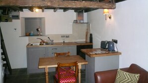A compact kitchen with a dining area, wooden beams, a kettle, and a small refrigerator. - Cosy, romantic fellside cottage hidden in the Glencoyne valley (Glenridding)