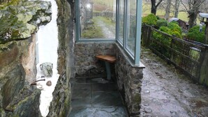 A narrow stone corridor with a bench, a window overlooking a rural path, and a stone wall. - Cosy, romantic fellside cottage hidden in the Glencoyne valley (Glenridding)