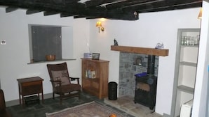 A cozy living room with a stone fireplace, wooden furniture, and a bookshelf. - Cosy, romantic fellside cottage hidden in the Glencoyne valley (Glenridding)