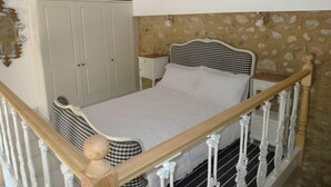 Ein Schlafzimmer mit kariertem Kopfteil, weißer Bettwäsche, einem hölzernen Bettgestell, einem weißen Kleiderschrank und einer Wand mit Steinmuster.