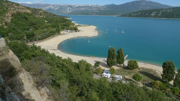 Eine Küstenlandschaft mit Strand, Booten und einem Bergpanorama im Hintergrund.