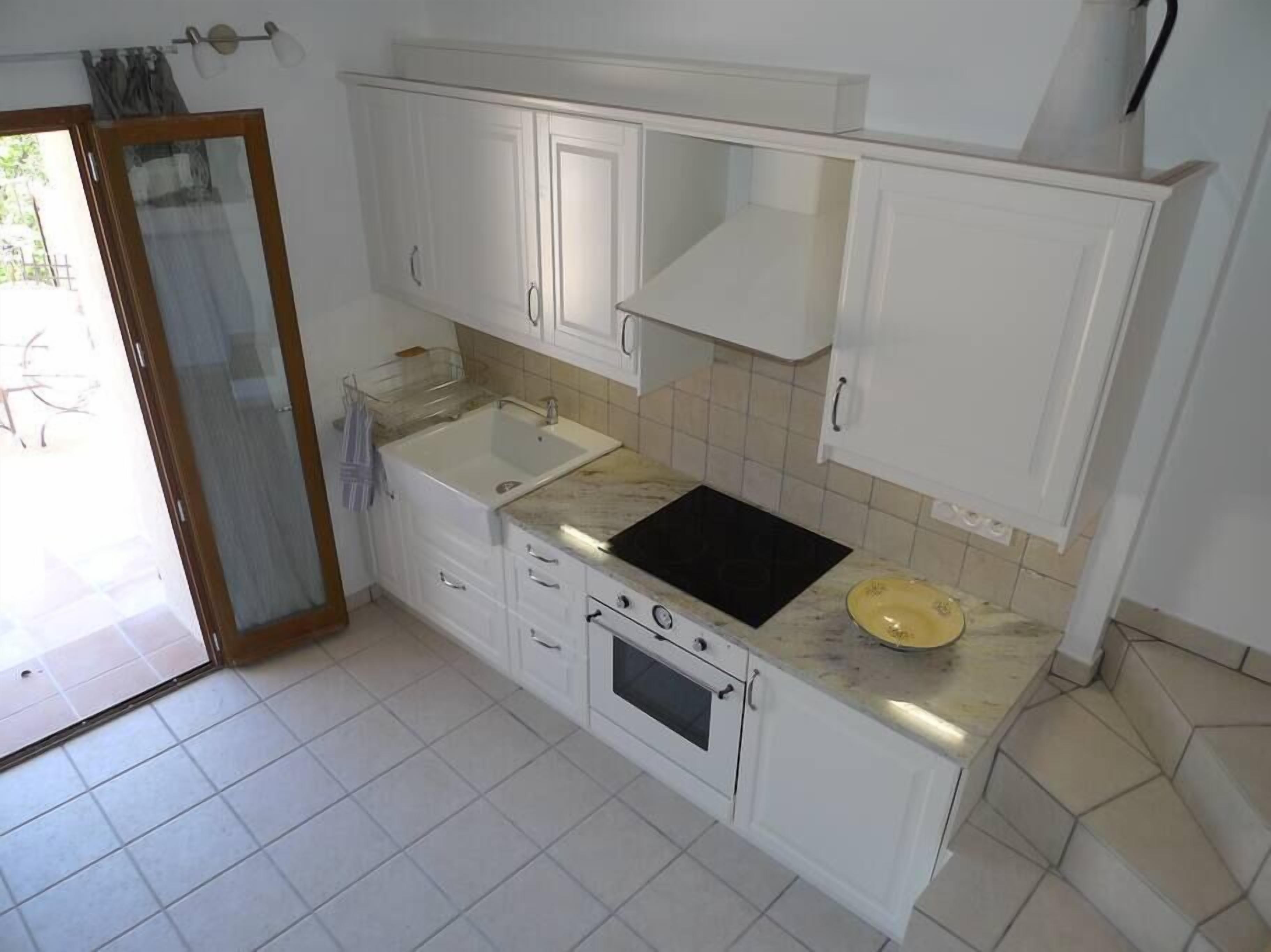 A kitchen with white cabinets, a sink, a stove, and a black countertop.