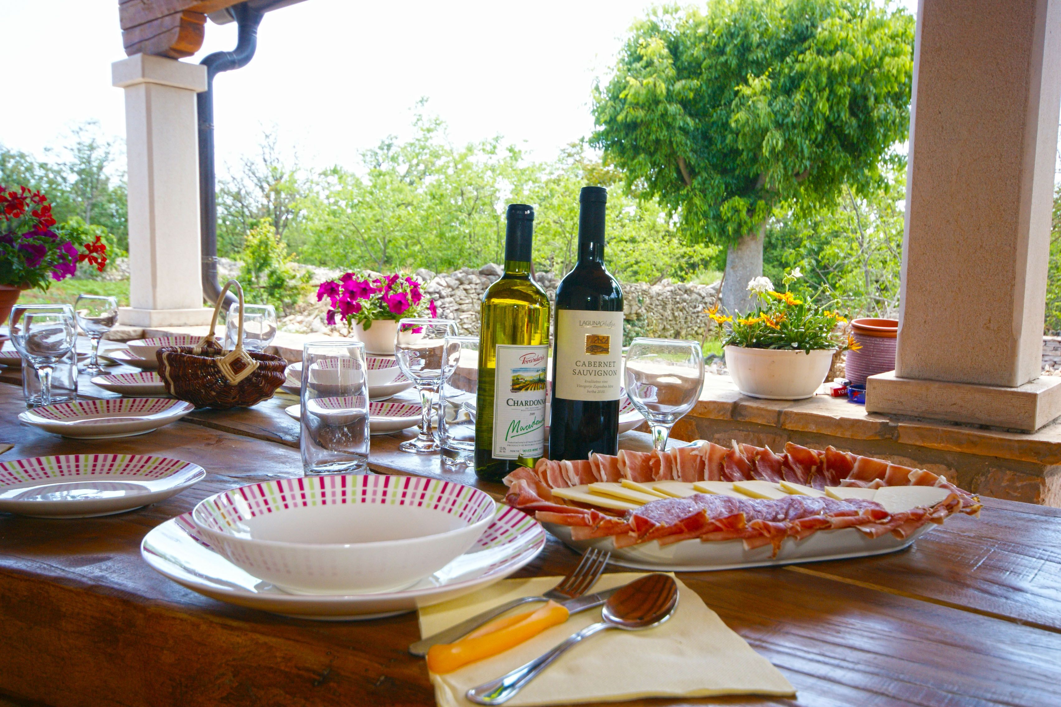Une table de jardin, dressée pour un repas en plein air, avec des assiettes, des verres, des couverts et des bouteilles de vin.