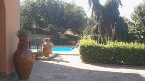 A stone pathway leading to a swimming pool surrounded by greenery and large vases.