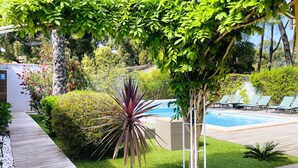 Een zwembadgedeelte met een houten terras, een groen gazon en een pergola begroeid met klimplanten.
