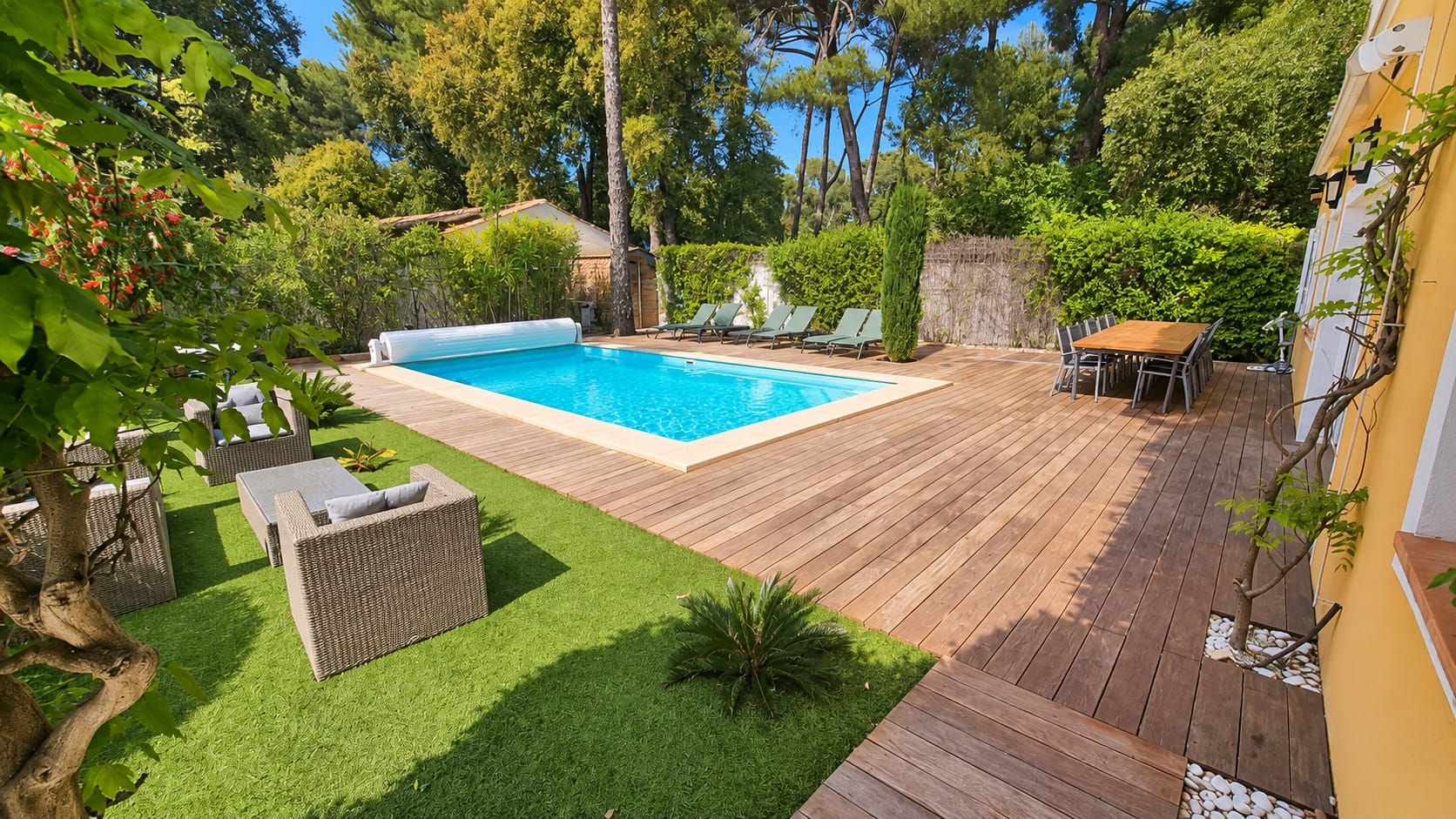 A backyard with a swimming pool, wooden deck, and outdoor furniture.