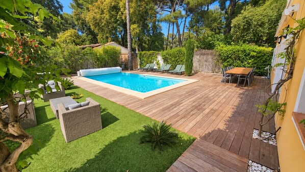 A backyard with a swimming pool, wooden deck, and outdoor furniture.