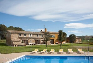 Un espace piscine avec des chaises longues et, en arrière-plan, un bâtiment en pierre.