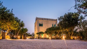 Un bâtiment avec une allée en gravier, entouré d’arbres et éclairé par un éclairage d’ambiance.