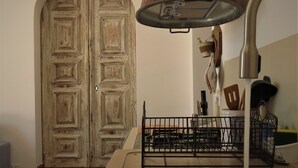 Una cocina con una puerta de madera rústica, una lámpara de metal y un lavabo con estante metálico.