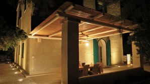 Un espacio de patio cubierto al aire libre con una mesa, sillas, una lámpara colgante y vistas del paisaje circundante.