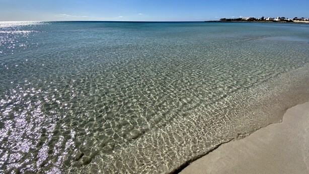 Una playa con aguas cristalinas y poca profundidad, y una orilla arenosa.
