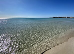 A beach with clear shallow water and a sandy shore.