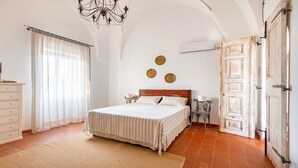 Un dormitorio con cama, cómoda, mesita de noche, candelabro, puerta y aire acondicionado instalado en la pared.