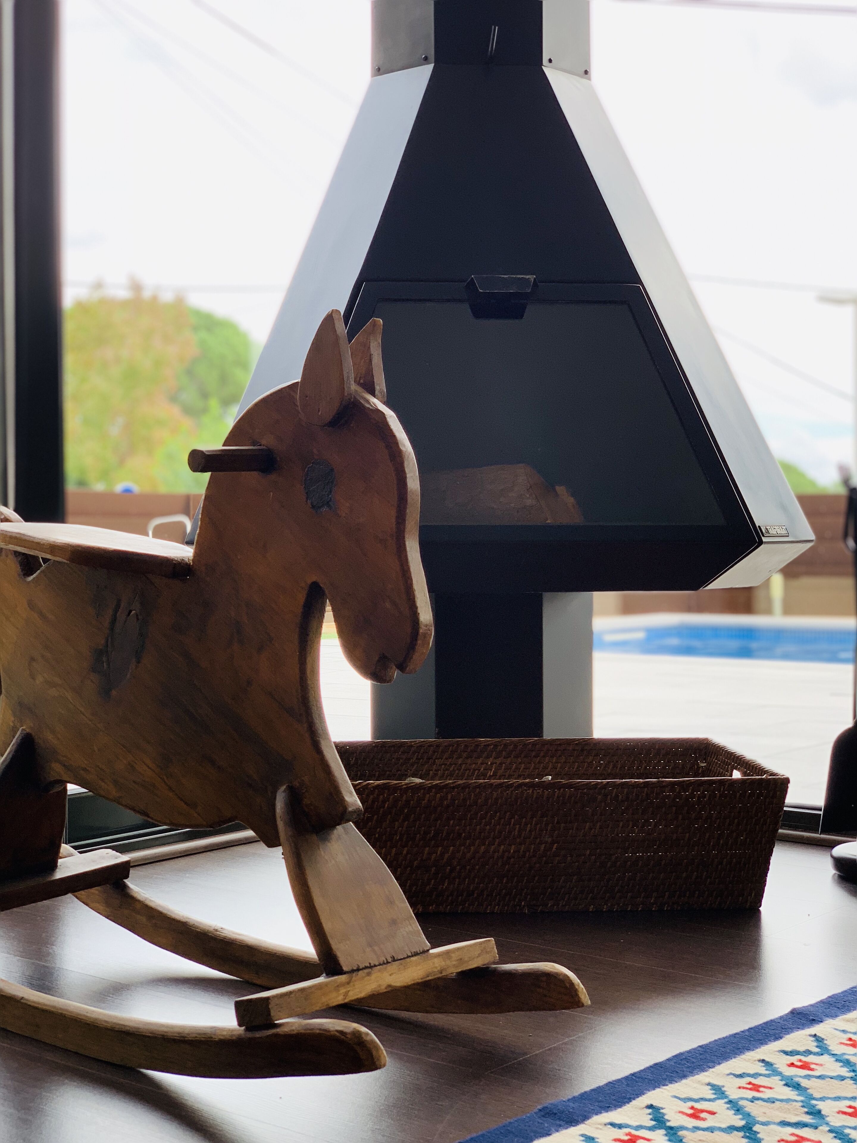 Un cheval à bascule en bois, placé à côté d’un barbecue extérieur moderne, avec une piscine en arrière-plan.