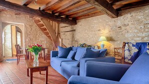 Una habitación rústica con pared de piedra, vigas de madera, un sofá azul, una mesa de madera con un florero y una lámpara.