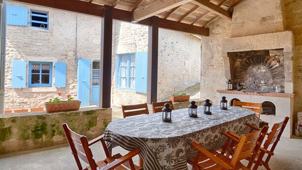 Un espacio de comedor al aire libre rústico, con pared de piedra, vigas de madera y chimenea de ladrillo.