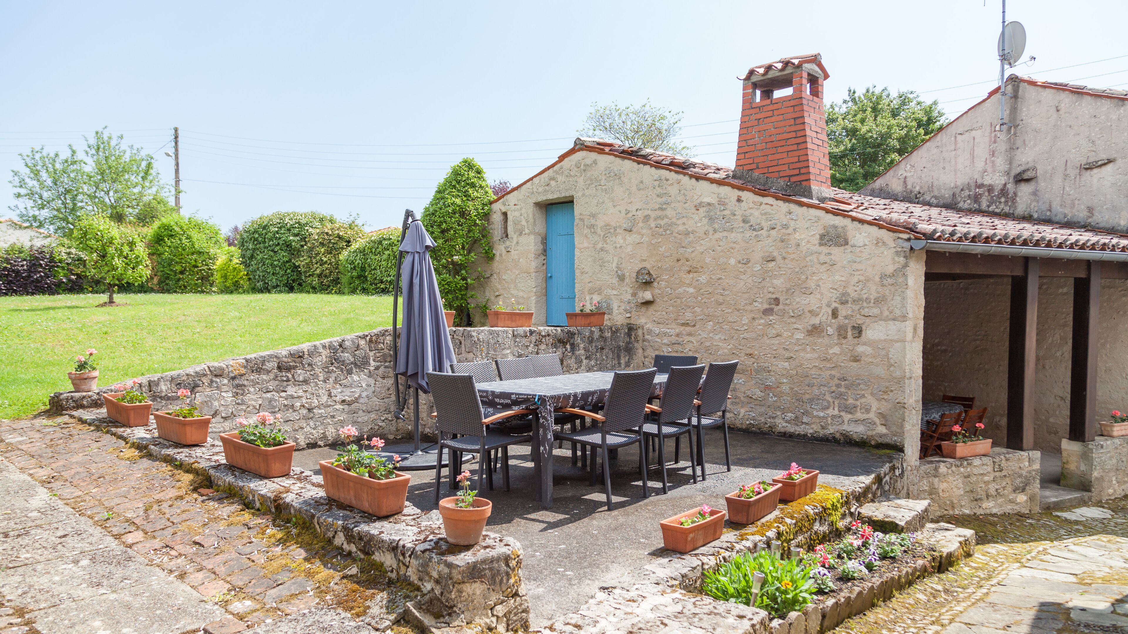 A stone patio with a table and chairs, surrounded by potted plants.