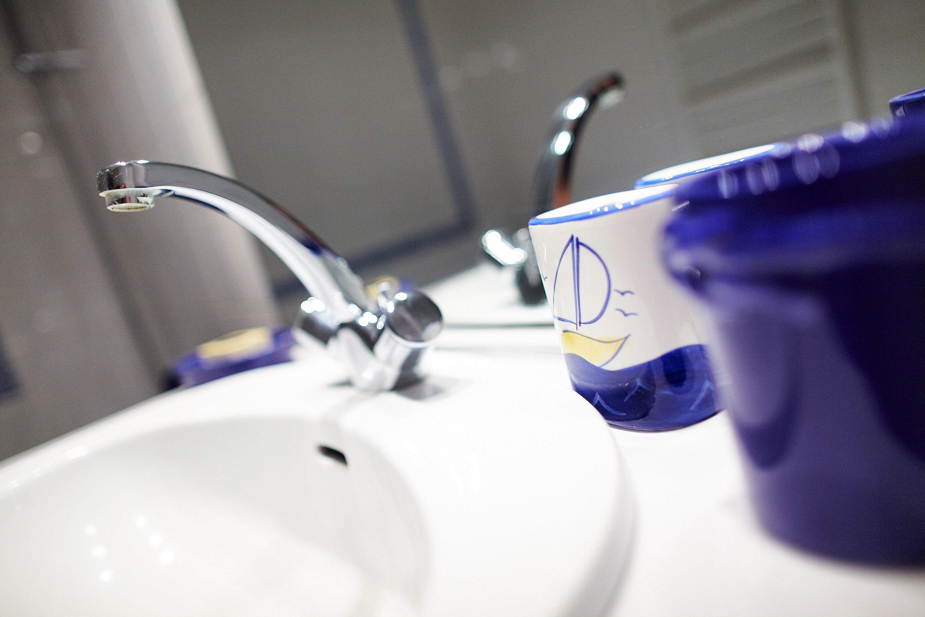 Un lavabo de salle de bain avec un robinet chromé et une tasse bleue ornée d’un visage souriant jaune.