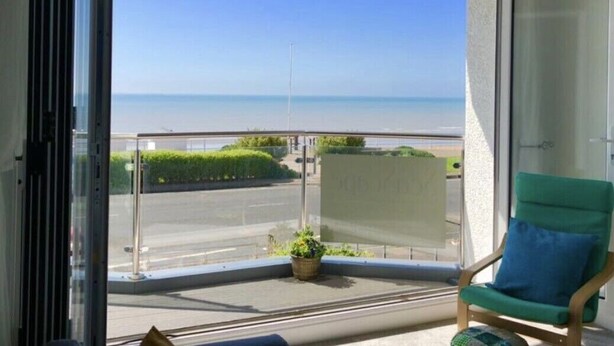 Un balcó amb una vista despejada del mar, una cadira verda i una planta en test.