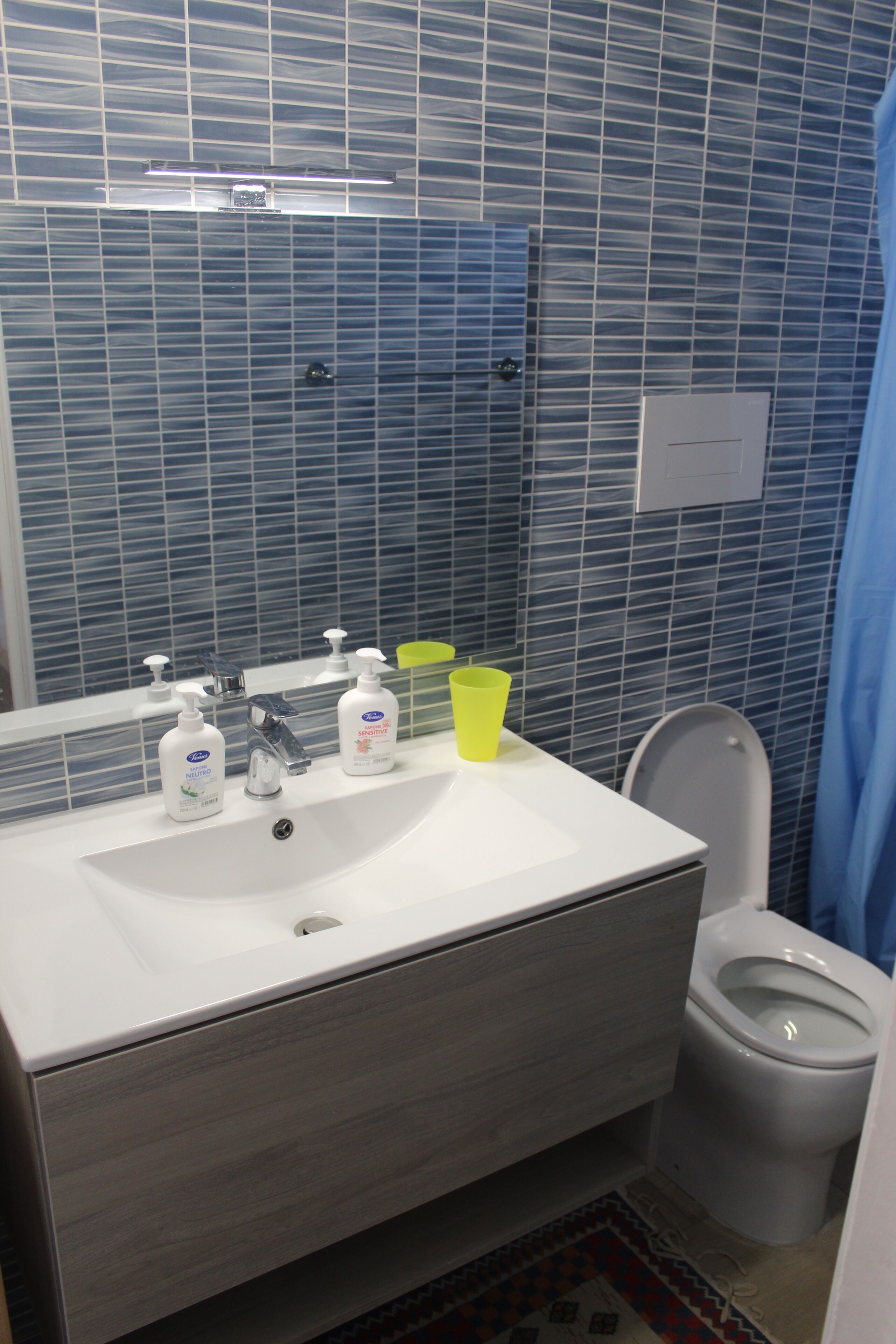 Ein Badezimmer mit einem weißen Waschbecken, zwei Seifenspendern, einem Spiegel und einer Toilette.