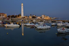 Un port où sont amarrés de nombreux bateaux, un phare imposant et des bâtiments qui bordent la promenade.