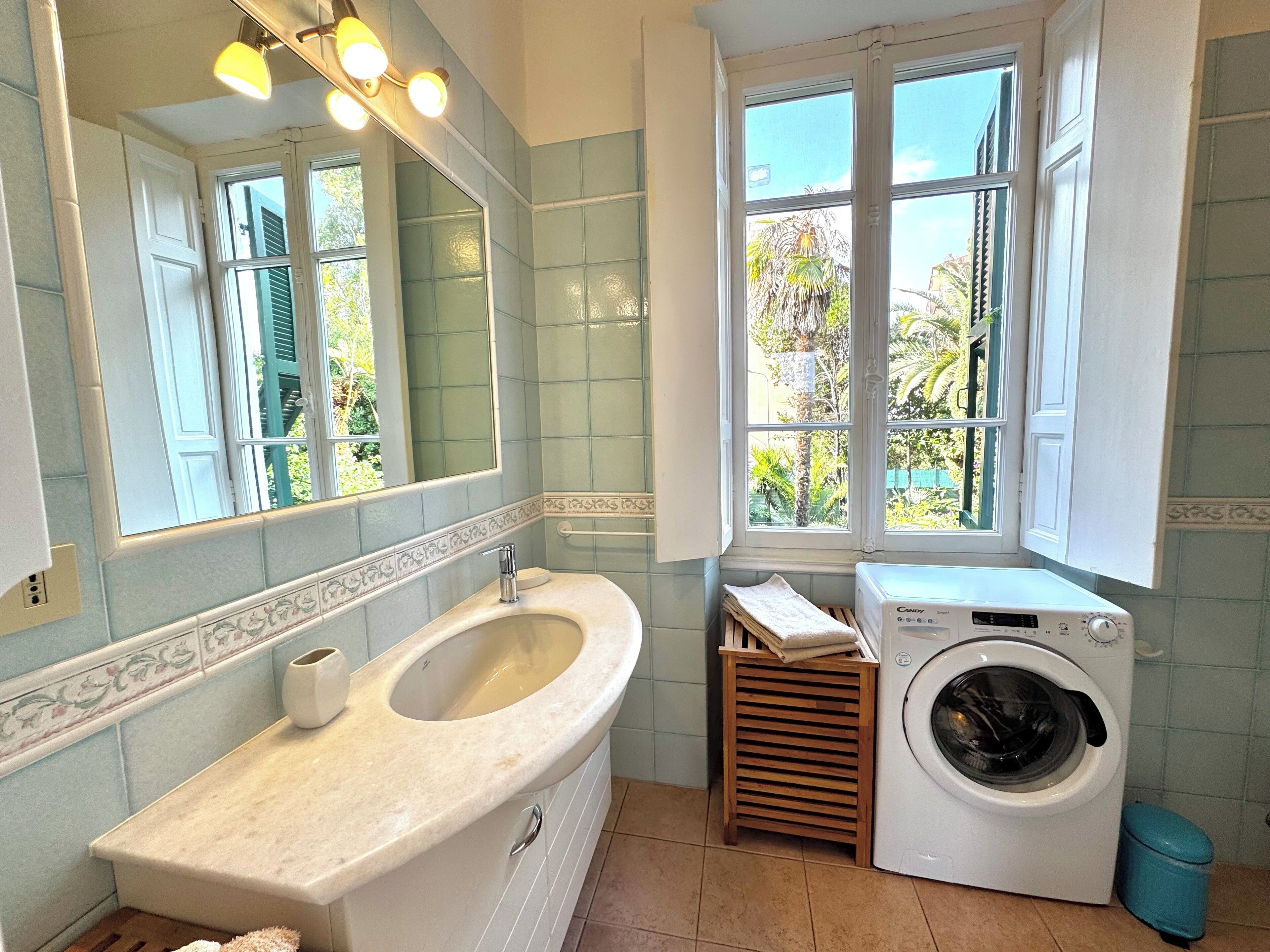 A bathroom with a sink, mirror, window, and washing machine.