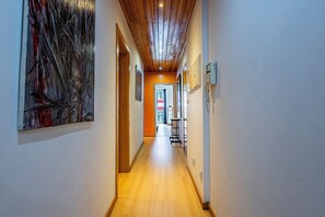 A hallway with wooden flooring, a ceiling with exposed beams, and a painting on the left wall.