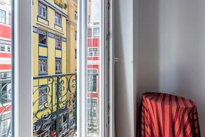 A balcony with a view of colorful buildings, a metal railing, and a chair with a striped cover.