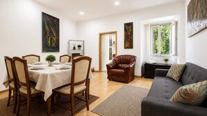 Ein Essbereich mit Tisch für vier Personen, ein Ledersessel, eine gepolsterte Couch mit gemusterten Kissen und Kunstwerken an den Wänden.