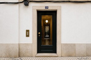 A black door with a brass plate and a number '19' above it, set in a beige wall with a tiled floor.