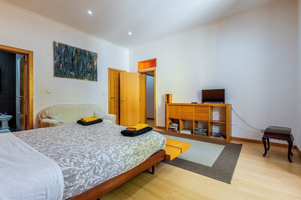 A bedroom with a bed, a wooden cabinet with a TV, and a bathroom visible through an open door.