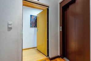 A hallway with a wooden floor, a door with a brown finish, and a wall-mounted light switch.