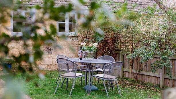 Eine Terrasse mit Tisch und Stühlen, einer Blumenvase und einer Weinflasche.