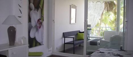 Un dormitorio con cama, una silla, una mesita, un espejo y vistas a un balcón exterior con sillas.