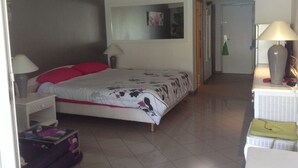 Quarto com cama, duas luminárias de cabeceira, ar-condicionado fixado na parede, porta para outro cômodo e uma mesinha com abajur.