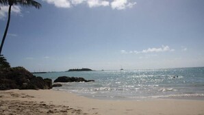 Uma praia com águas azul-claras, areal arenoso e uma ilha ao longe.