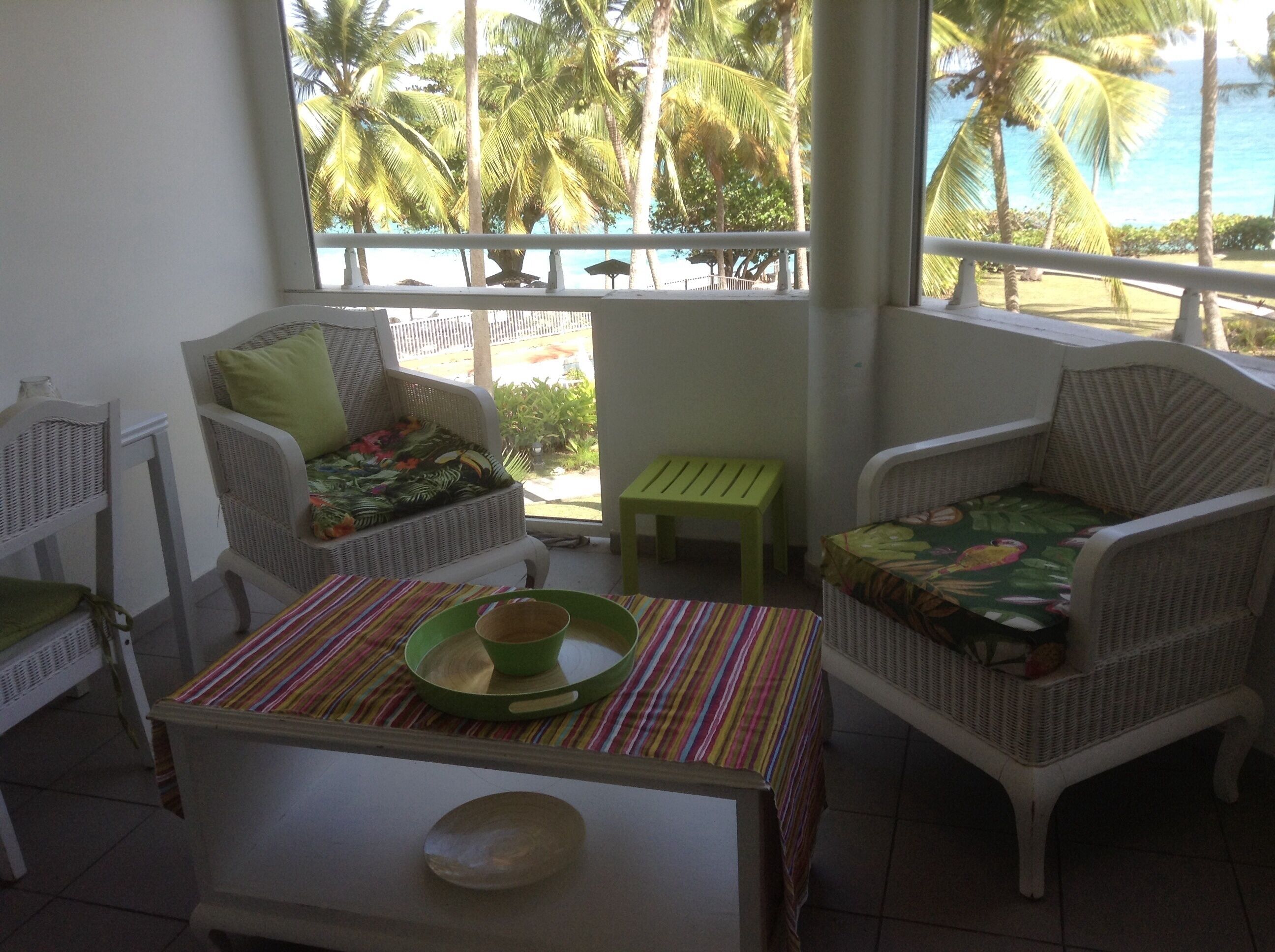 A room with wicker furniture, a striped table, and a view of palm trees and the ocean.