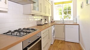 A modern kitchen with white cabinets, a gas stove, a dishwasher, and a window with a view of greenery. - Great location - sleeps up to five guests, just moments from the beach and town (Eastbourne)