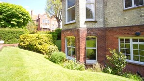 A corner brick building with large windows, a well-maintained lawn, and surrounding greenery. - Great location - sleeps up to five guests, just moments from the beach and town (Eastbourne)